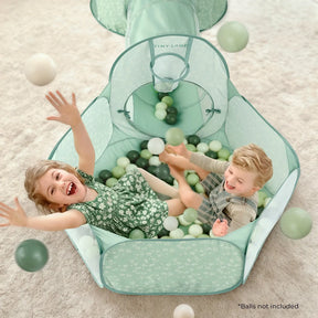 Two young children play and laugh in the mint green Tiny Land® Compact Adventure 3-in-1 Play Tunnel, tossing white and green balls. The ball pit features soft pastel colors and a floral pattern. Text reads: "*Balls not included.|green