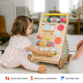 A toddler sits on the floor in a cozy indoor setting, playing with the Tiny Land® Premium Natural Wooden Activity Walker by Tiny Land, a colorful toy featuring beads, gears, and blocks. Icons below highlight its benefits for motor skill development.