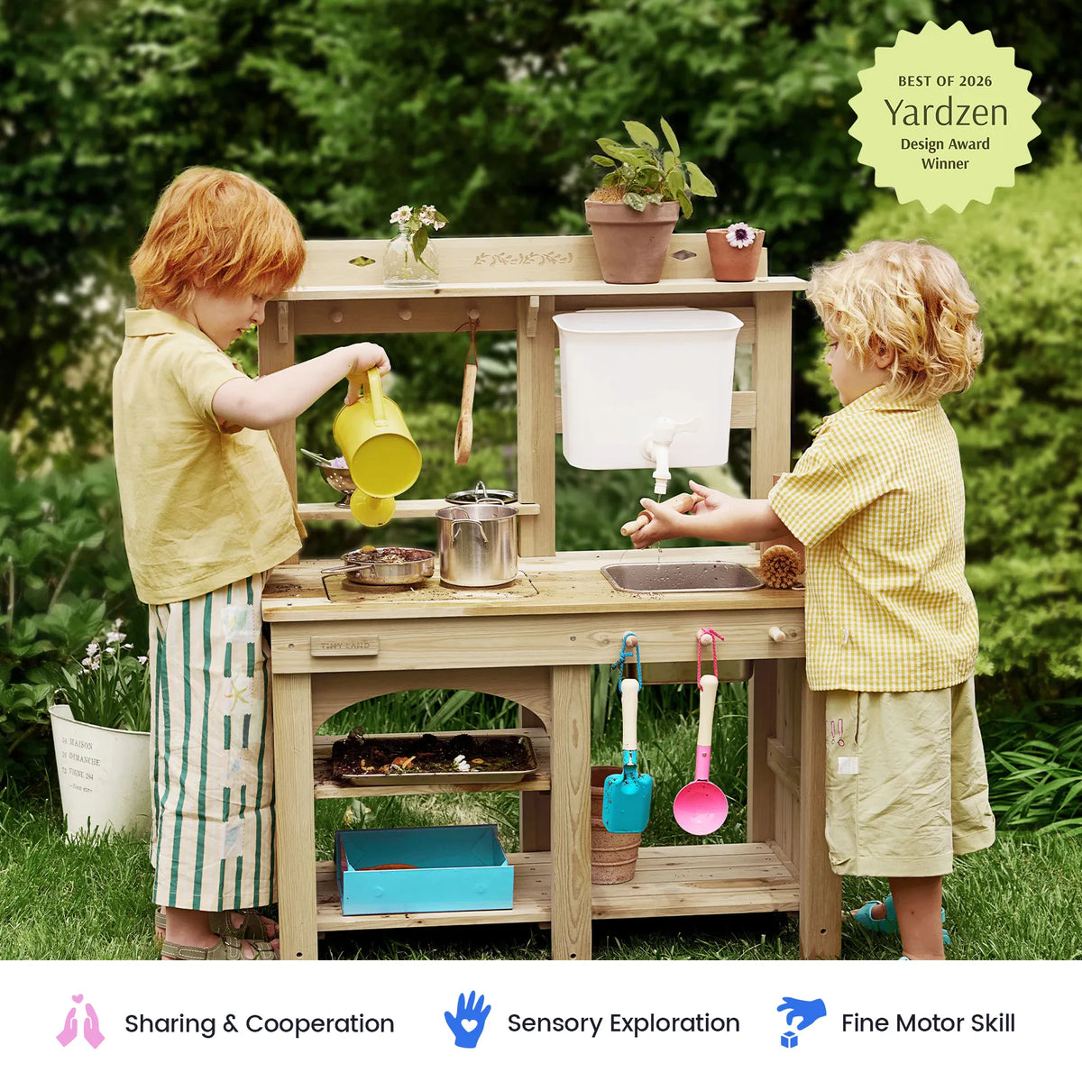 Two young children play at the Tiny Land® Mud Kitchen - DuoPlay Outdoor Play Kitchen for Kids by Tiny Land, pouring water and using utensils. Set in a grassy yard with potted plants, the vibrant kitchen encourages kids to engage in sensory play, exploration, and interactive outdoor fun.
