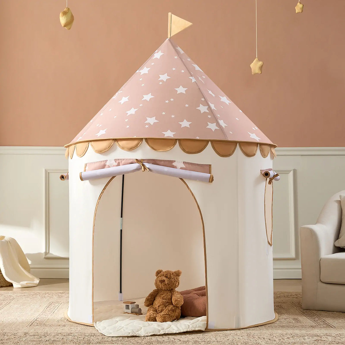 The Tiny Land® Kids Tent by Tiny Land features a pink, star-patterned roof with a flag, an open entrance, and includes a cozy mat for play. A brown teddy bear sits inside, perfect for indoor fun in rooms with pale walls and beige decor.|Brown