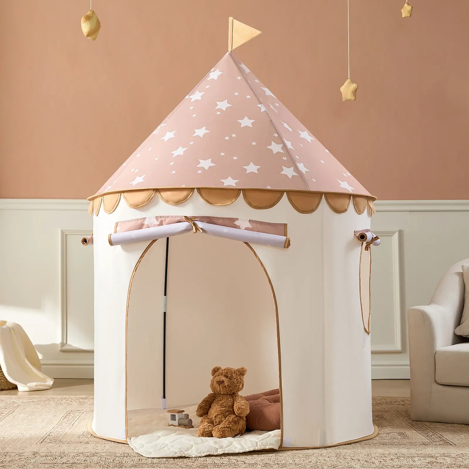 The Tiny Land® Kids Tent by Tiny Land features a pink, star-patterned roof with a flag, an open entrance, and includes a cozy mat for play. A brown teddy bear sits inside, perfect for indoor fun in rooms with pale walls and beige decor.|Brown