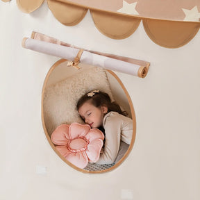 A young girl sleeps in the Tiny Land® Kids Tent—an indoor tent for toddlers—hugging a pink flower-shaped pillow and resting on a fluffy white cushion. The tent by Tiny Land features a round window with rolled-up fabric and scalloped star edges.|Brown