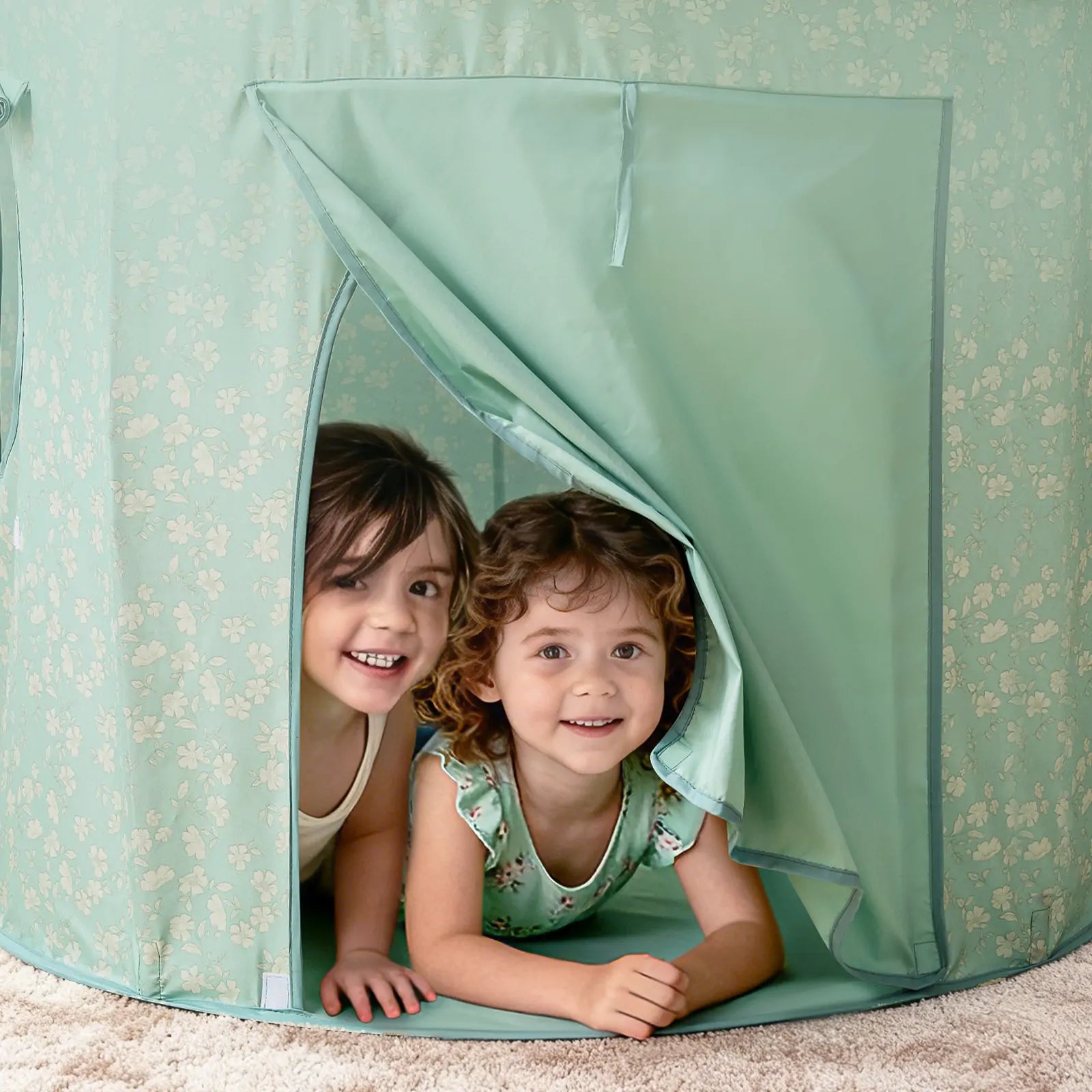 Two young children smile as they lie on their stomachs inside the Tiny Land® Tiny Sprout Castle Tent, peeking out through the open flap onto a beige carpet.|Green