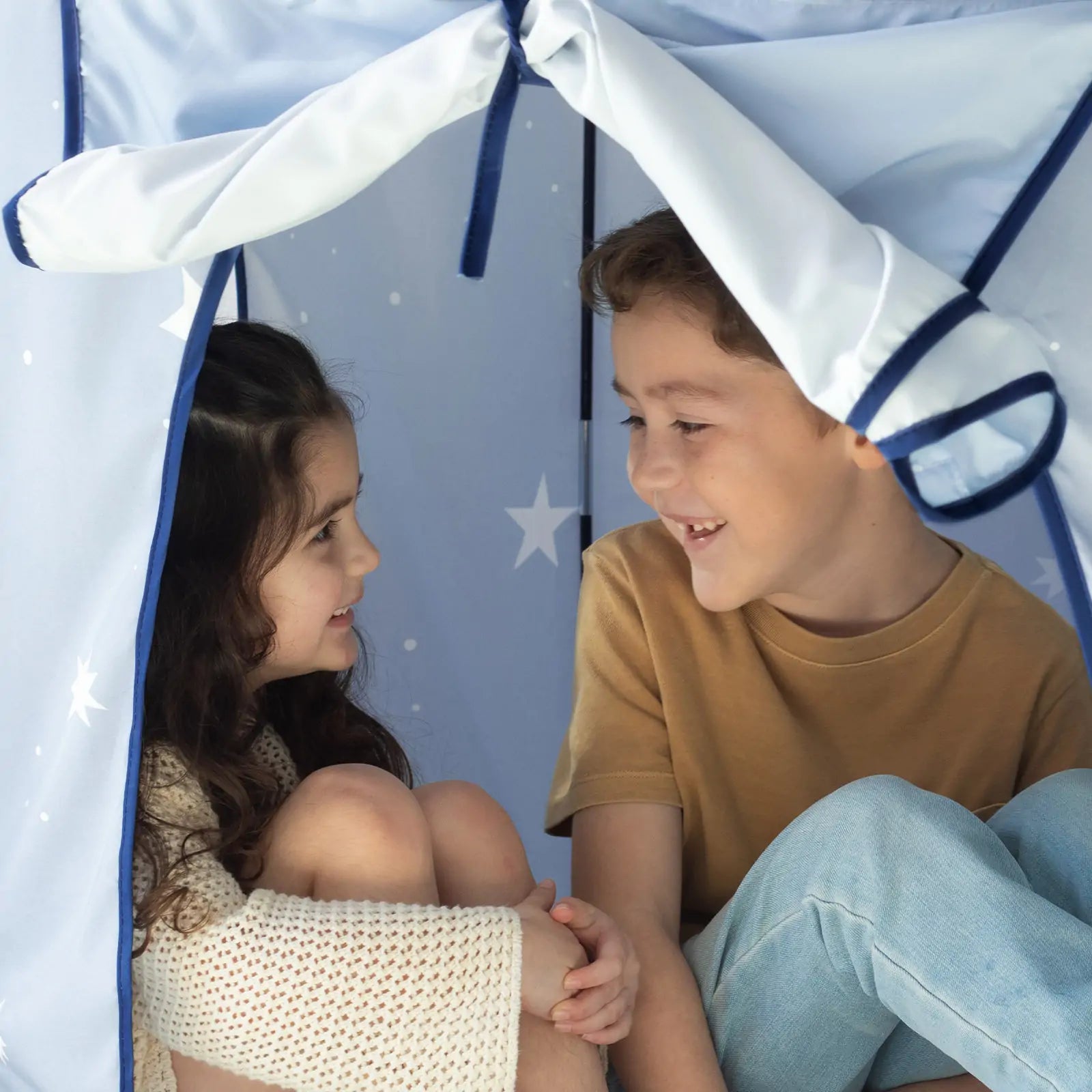 Two children smile as they sit inside the Tiny Land® Kids Tent – Indoor Tent for Toddlers by Tiny Land, a cozy blue play tent with white stars, perfect for playful moments in their indoor playhouse.|Blue