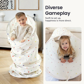 Two young children enjoy the Tiny Land® Adventure Play Tunnel in a sunlit room. The boy stands inside the collapsible, polka-dotted tunnel by Tiny Land, while the girl crawls through, both smiling and having fun. Text reads: Diverse Gameplay.|Colorful Dots