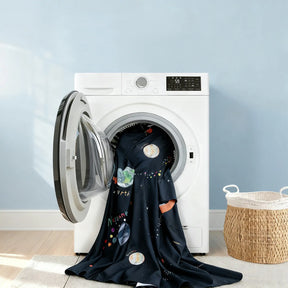 A front-loading washer holds a Tiny Land® Kids Bed Tent by Tiny Land, its colorful planets and stars fabric draped out, perfect for inspiring a fun indoor tent or kids' hideaway. A woven laundry basket rests nearby against a light blue wall.|SPACENEST