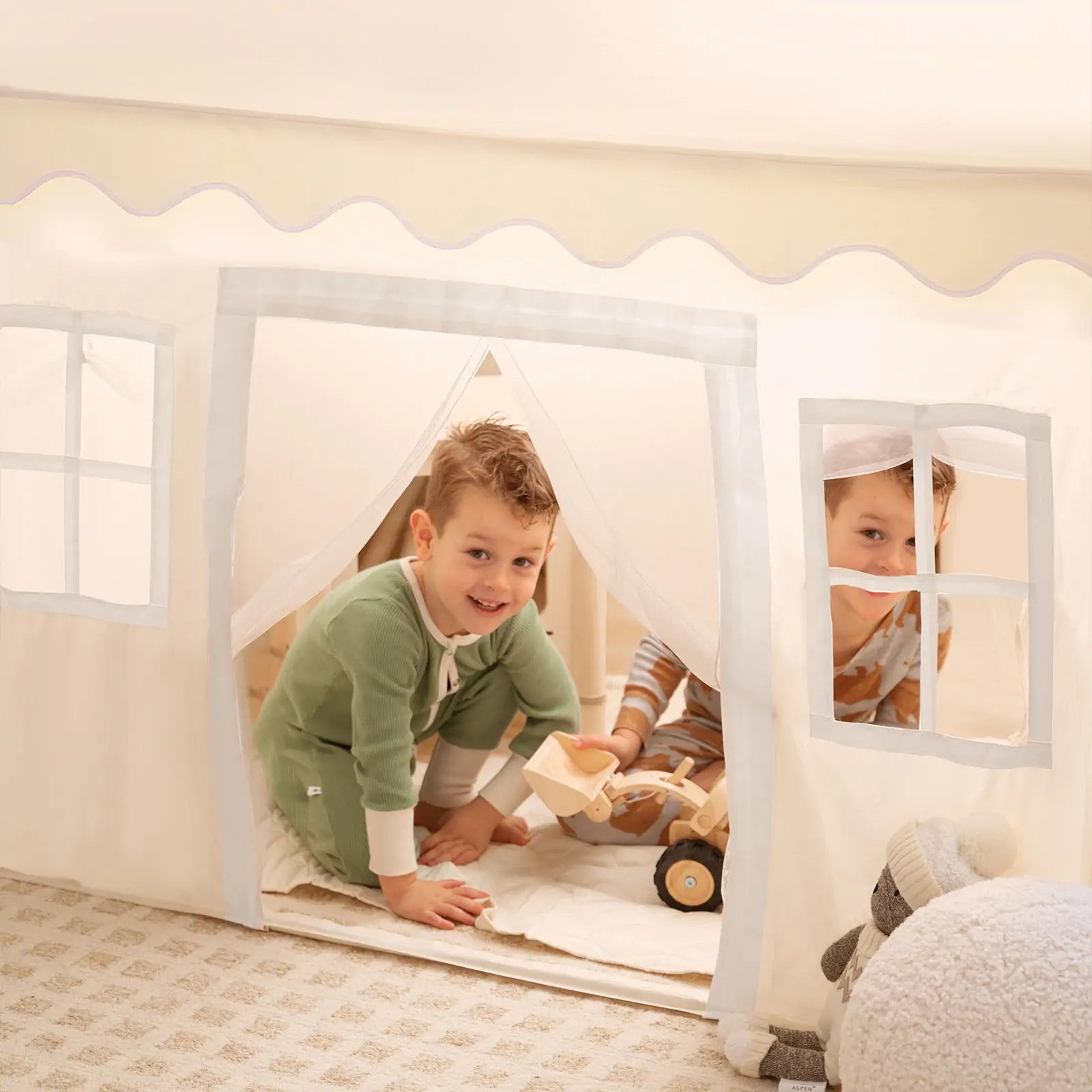 Two children play in the Tiny Land® Playhouse Tent – Natural Cream Indoor Tent for Kids. One crawls out while the other peeks inside. A toy truck and plush sheep are nearby, adding to the fun from Tiny Land|white