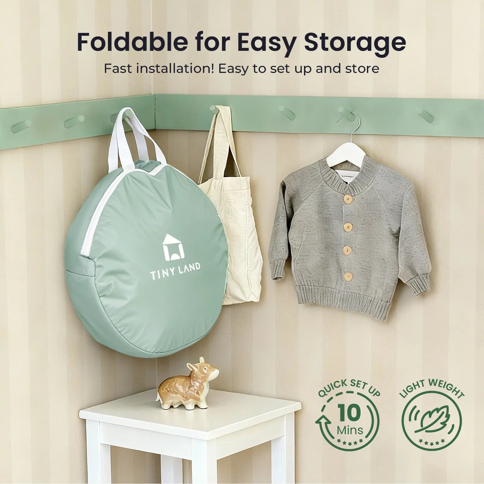 A sage green Tiny Land® Compact Adventure 3-in-1 Play Tunnel (no balls) hangs on a wall hook next to a child’s gray sweater, with a decorative hippo below. Lightweight and easy to set up—perfect for storing your play tunnel.|green