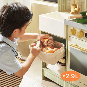 A young child wearing an apron places a fabric basket, which holds about 2.9 liters, into the sink area of the Tiny Land® BistroSwitch Play Kitchen by Tiny Land—part of a fun pretend play kitchen set for kids.|Green
