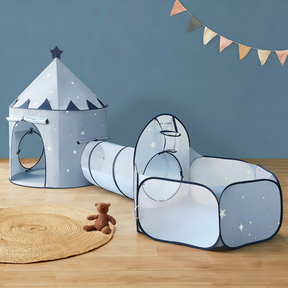 The Tiny Land® Compact Adventure 3-in-1 Play Tunnel With no Balls - Blue, shaped like a starry castle and connected to a tunnel and ball pit, sits on a wooden floor beside a round rug, a brown teddy bear, and colorful pennant banners above.|blue