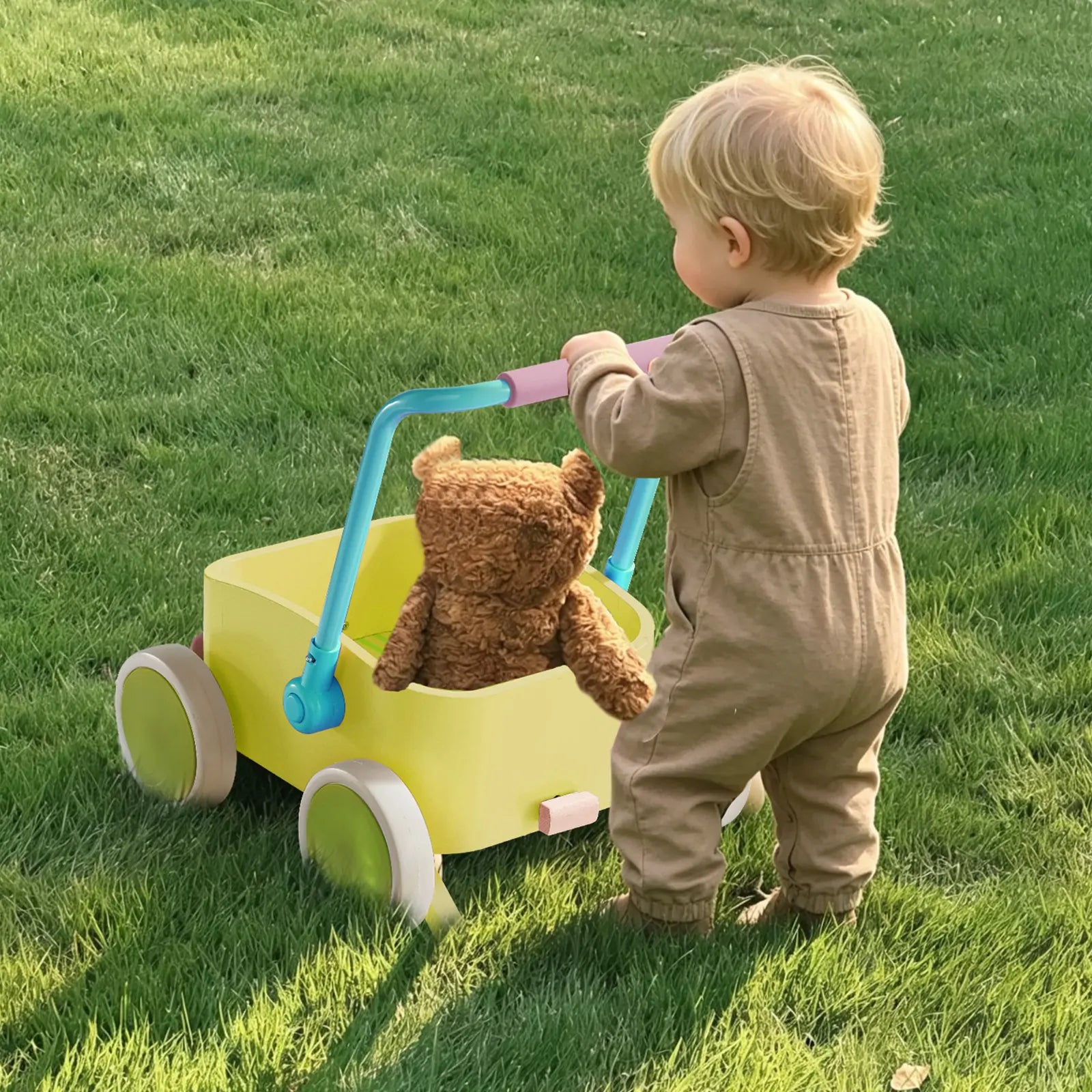 A toddler in a brown jumpsuit pushes the Tiny Land® 3-in-1 Wooden Baby Walker Wagon - Spring Color by Tiny Land, featuring adjustable speed control and a brown teddy bear inside, across green grass using its blue handle.