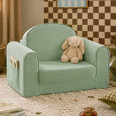 The Tiny Land® GentleSnug Kids Sofa Chair in light green, featuring a side pocket holding a soft beige bunny, sits on a carpeted floor in a cozy room with books and toys nearby.