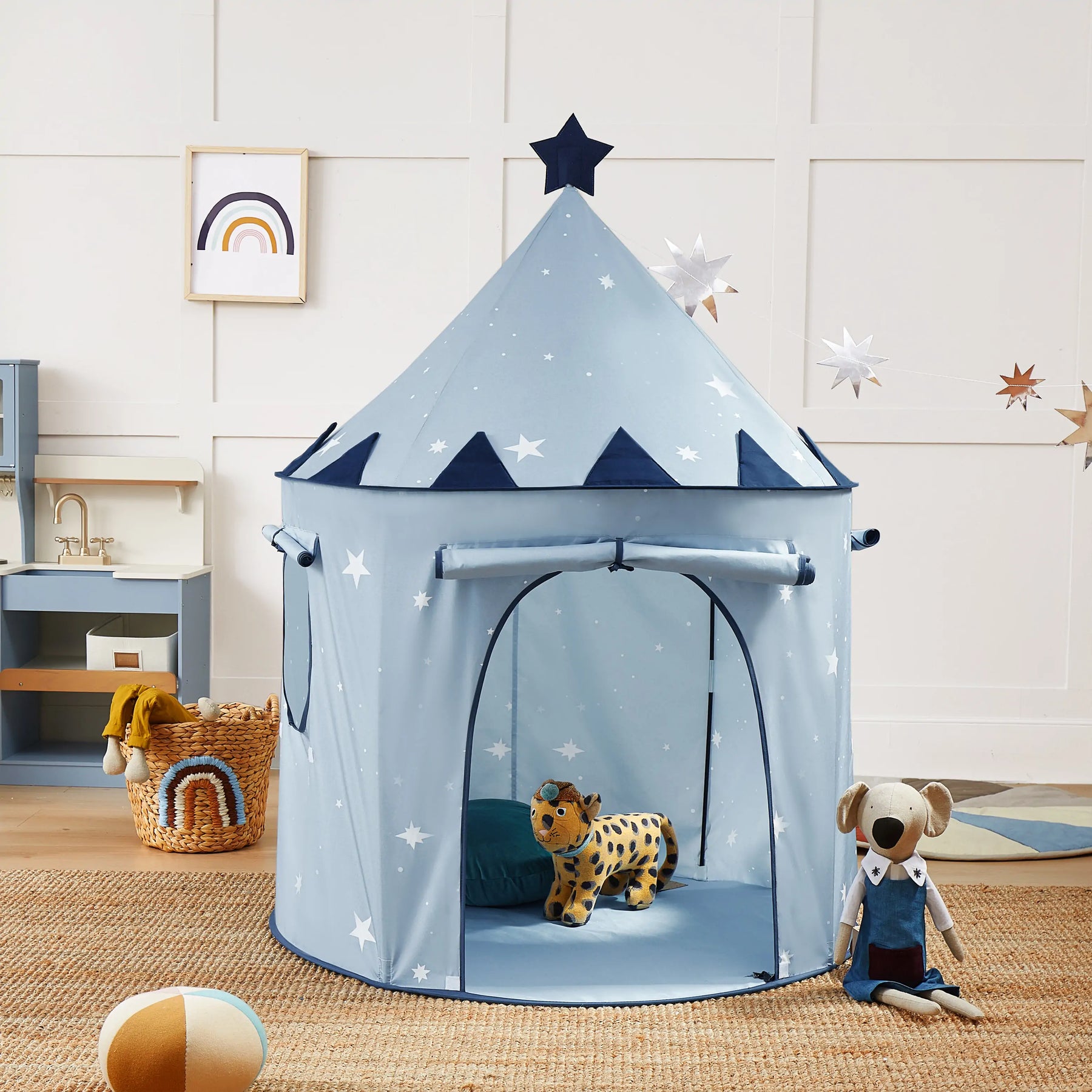 The Tiny Land® Kids Tent – Indoor Tent for Toddlers by Tiny Land, featuring blue fabric with white stars and a star topper, is set in a playful kids’ room filled with plush toys, colorful decor, shelves, and wall art.|Blue