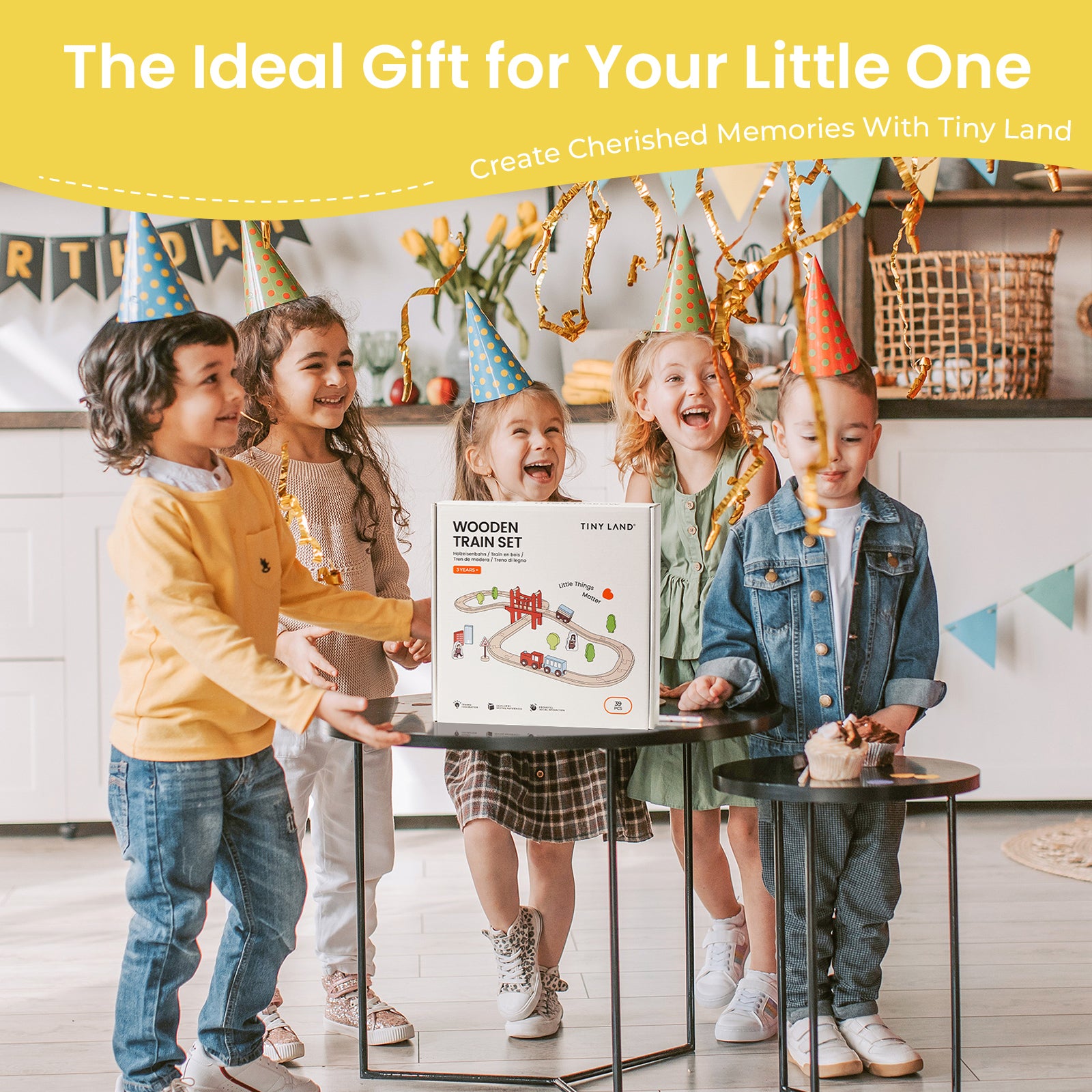 Four children in party hats smile around a gift box labeled "Tiny Land® Wooden Train Set for Children 39 Pcs" by Tiny Land, placed on a table. The festive background features colorful decorations and golden streamers.|39 Pcs