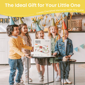Four children in party hats smile around a gift box labeled "Tiny Land® Wooden Train Set for Children 39 Pcs" by Tiny Land, placed on a table. The festive background features colorful decorations and golden streamers.|39 Pcs