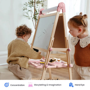 Two young children are engaged with the Tiny Land® Pink Magnitales Easel & Paper Roll Set in a bright room. One child draws while the other observes, with art supplies neatly arranged on a pink tray. Three icons below emphasize the benefits of concentration, storytelling & imagination, and hand-eye coordination provided by this Tiny Land easel set.|Pink