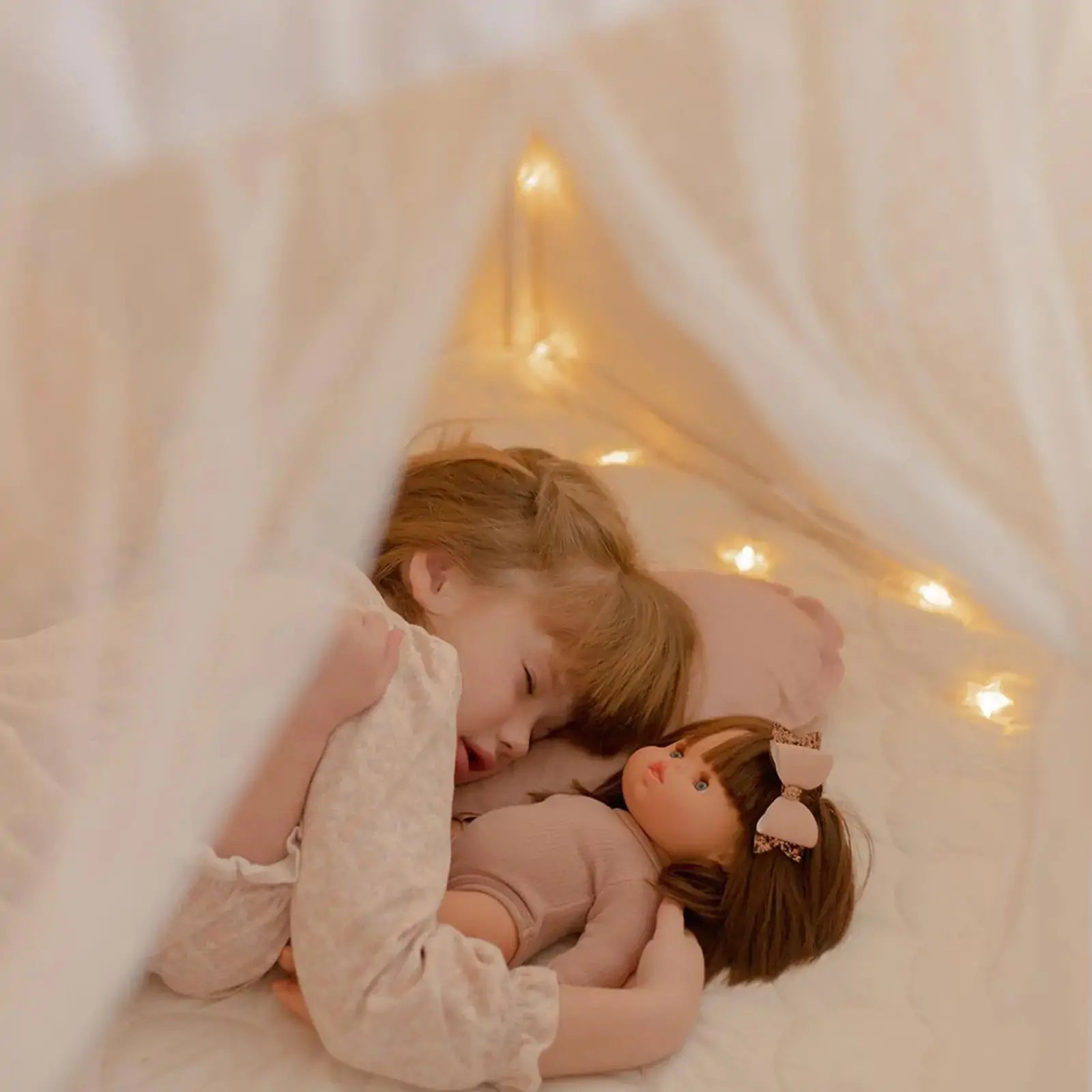 A young child relaxes under the Tiny Land Bright Play & Art Set—featuring a colorful easel and a cream playhouse with lights—enjoying the warm glow and cozy, dreamy atmosphere created by soft fairy lights inside the tent|white