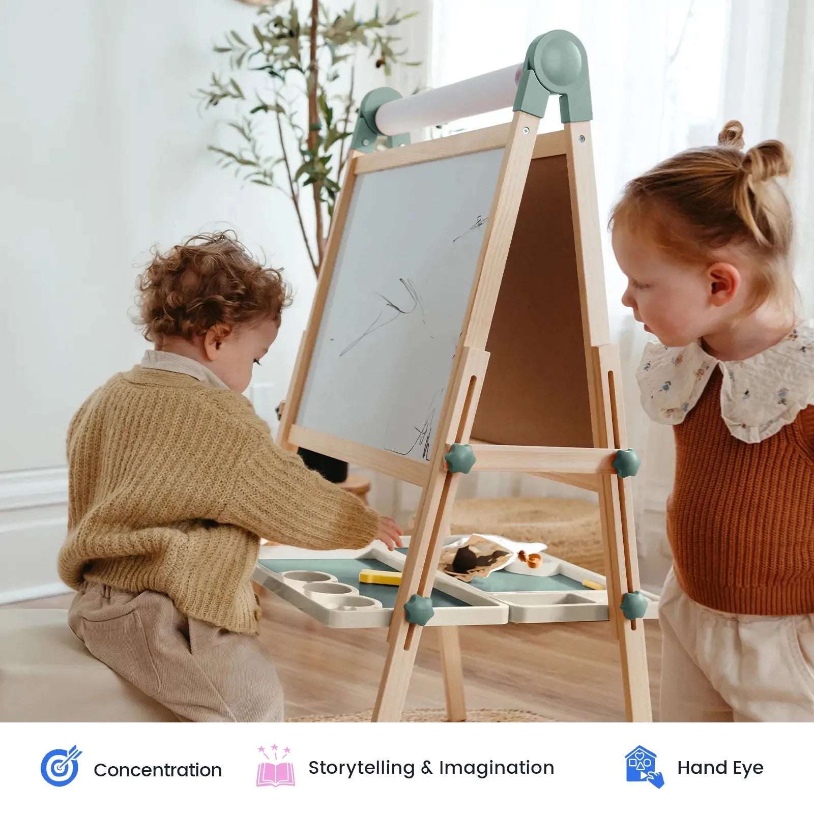 Two young children draw on the Tiny Land® Pink Magnitales Easel & Paper Roll Set in a bright room, fully focused and engaged as they create. Art supplies surround them, supporting their play. Icons below highlight key benefits: concentration, storytelling & imagination, and hand-eye coordination.|Green