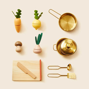 The Tiny Land® Mediterranean Play Kitchen by Tiny Land includes a cutting board, knife, spatula, mushroom, three veggies, two gold pots with lids, and a gold ladle—perfectly arranged on a beige background|Mediterranean