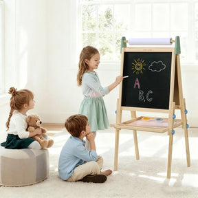 Three young children are in a bright room. One girl uses the Tiny Land® 3-in-1 Art Easel for Kids - Morandi by Tiny Land to draw, while another girl hugs a teddy bear and sits on the floor with a boy watching her.|green