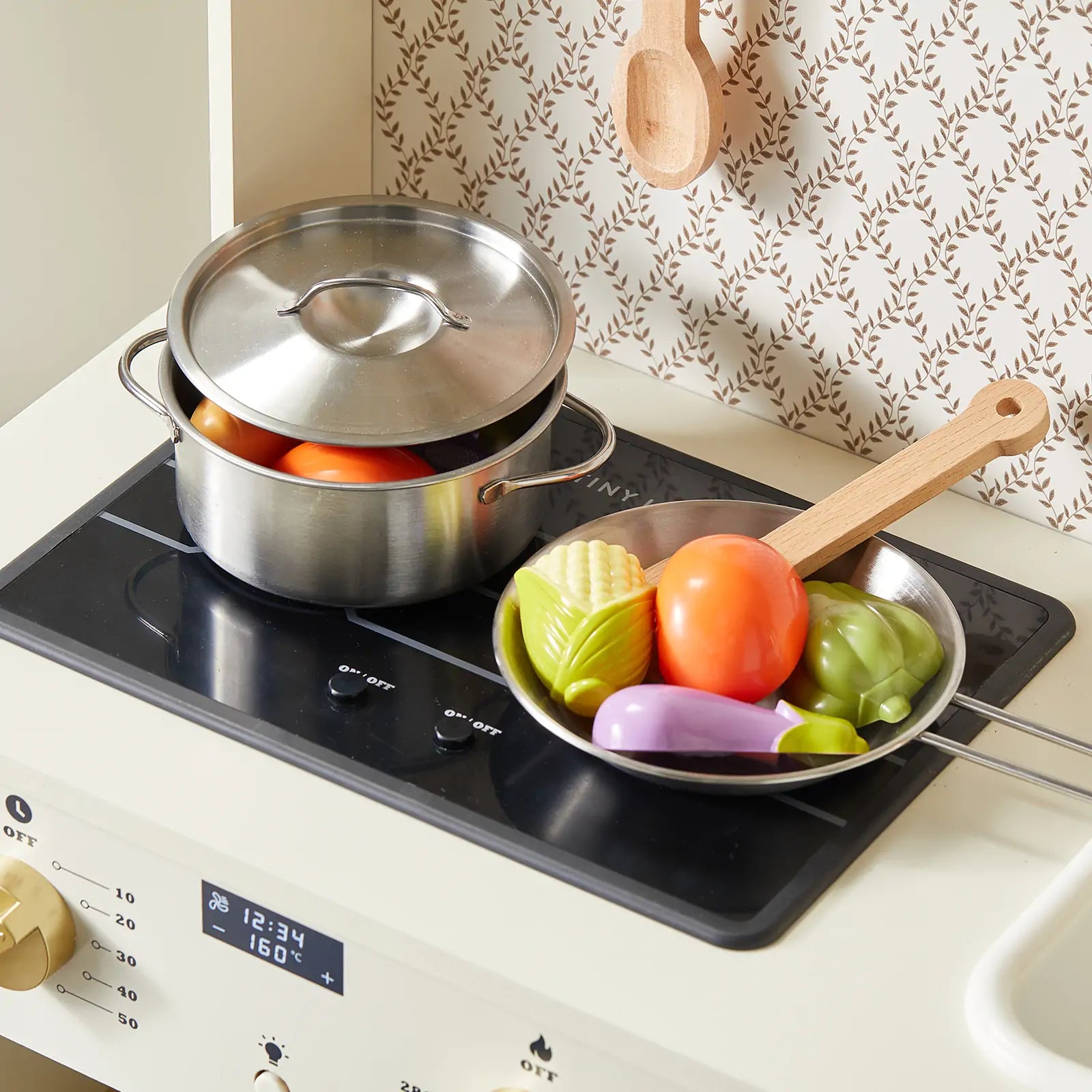 The Tiny Land® Farm-to-Table Play Set by Tiny Land features an interactive wooden kitchen with a stovetop, metal pot and lid, frying pan with toy veggies (corn, tomato, eggplant, green pepper), wooden spoon, fridge for storage & organic food collection.