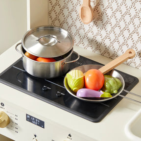 The Tiny Land® Farm-to-Table Play Set by Tiny Land features an interactive wooden kitchen with a stovetop, metal pot and lid, frying pan with toy veggies (corn, tomato, eggplant, green pepper), wooden spoon, fridge for storage & organic food collection.