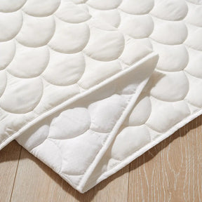 A close-up of a white quilted mattress pad with a circular stitched pattern, folded neatly on a light wooden floor—perfect for adding comfort to the Tiny Land® Playhouse Tent by Tiny Land.|white