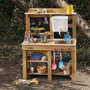The Tiny Land® Outdoor Mud Kitchen & Sand Play Set by Tiny Land stands in a garden, featuring toy pots, pans, utensils, colorful play food, sand toys, and baskets with pretend ingredients—ideal for outdoor fun among trees and greenery.