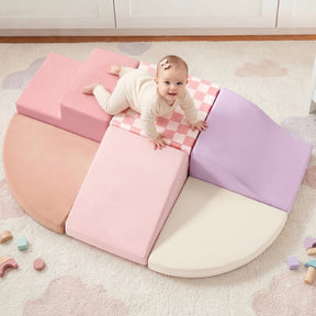 A baby in cream clothes with a pink bow crawls on the Tiny Land® PlayNest Climbing Blocks—a pastel pink, purple, and cream foam play set—surrounded by wooden toys and toddler climbing toys in a cozy nursery.