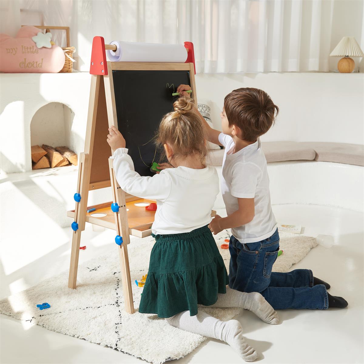 A girl and a boy kneel on a rug, drawing with chalk on the Tiny Land® 3-in-1 Art Easel & Paper Roll Set in a bright, cozy room with white decor and natural light.|red