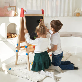 A girl and a boy kneel on a rug, drawing with chalk on the Tiny Land® 3-in-1 Art Easel & Paper Roll Set in a bright, cozy room with white decor and natural light.|red