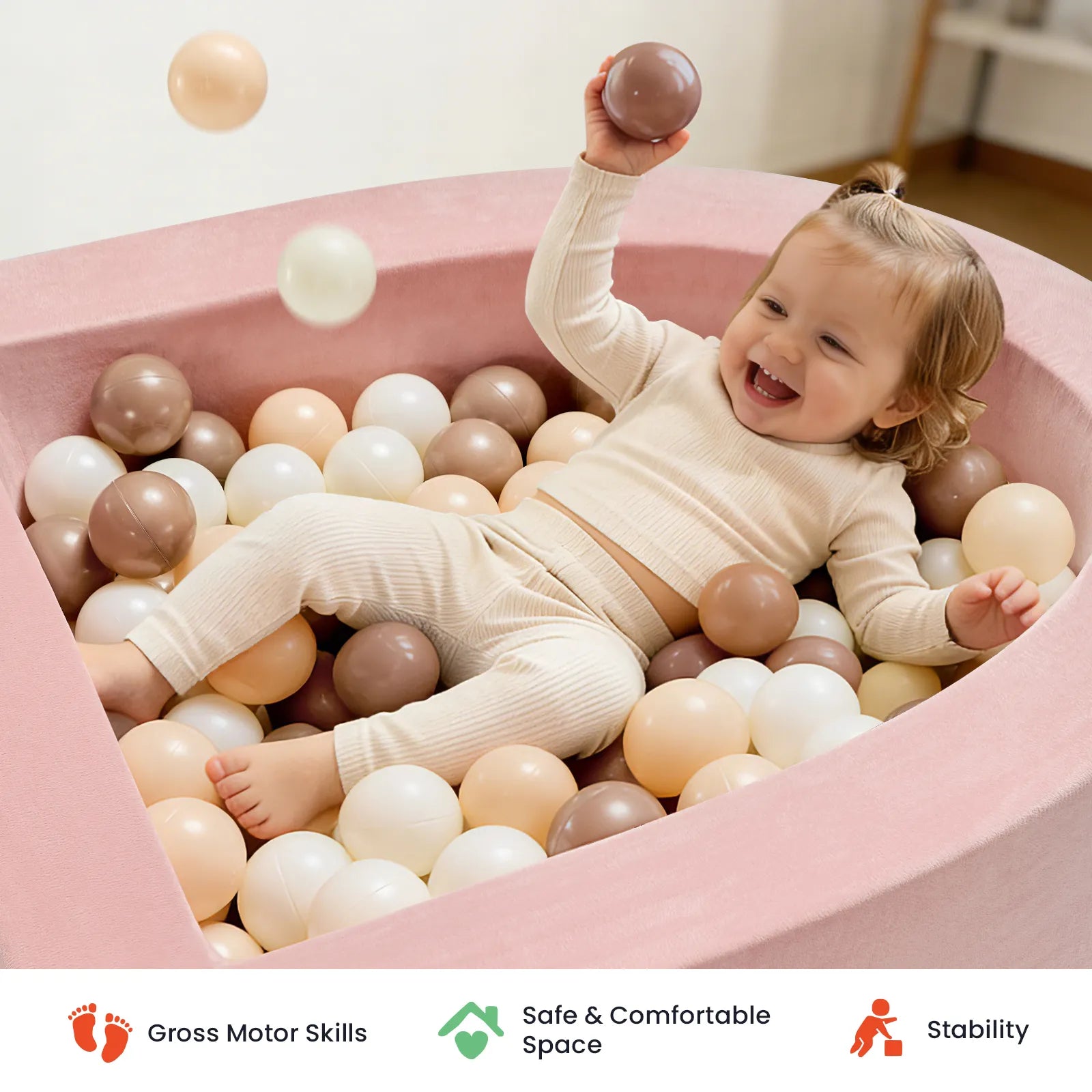 A cheerful toddler dressed in cream enjoys the Tiny Land® PlayNest Ball Pit with 200 Ocean Balls by Tiny Land, surrounded by a mix of white, beige, and brown balls. Icons below showcase gross motor development, a secure play space for toddlers, and enhanced stability.|Pink
