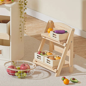 The Tiny Land® Play Kitchen Accessories – a versatile wooden rack for play food – organizes toy fruits and veggies in two crates, while a nearby white wire basket holds more toy apples and grapes for tidy kids’ room storage.