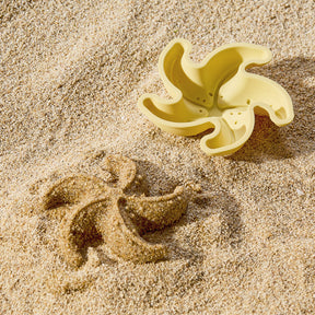 A yellow star-shaped mold from the Tiny Land® Sand-Buddies Sand Toy Set by Tiny Land sits on the sandy beach beside its matching impression.