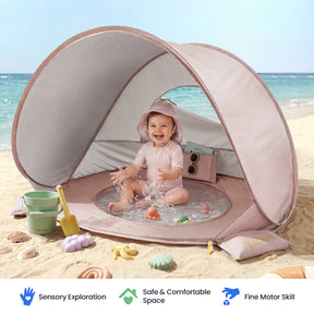 A smiling baby plays with water and toys inside the Tiny Land® 4-in-1 Tent: Beach Tent & Sand Toy Set by Tiny Land on a sandy beach. The open, portable tent is surrounded by a colorful sand toy set, bucket, and seashells. Three icons emphasize the sensory, safety, and motor skill benefits of the product.|Pink