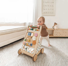 A baby is pushing the Tiny Land® Versatile Natural Wooden Baby Walker by Tiny Land, featuring colorful beads and shapes, in a bright living room with a sofa, toys, and a wall chart in the background|Morandi