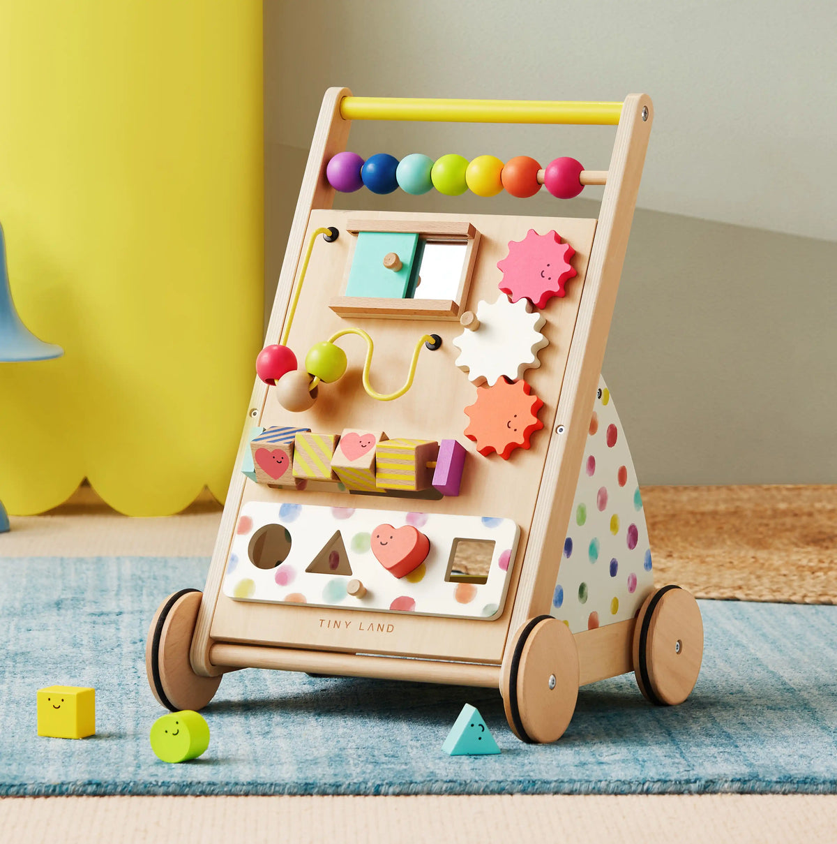 The Tiny Land Rainbow Baby Walker & Activity Cube Developmental Playset, a vibrant wooden walker with interactive beads, spinning gears, shape sorters, and sliding blocks for fine motor skills, rests on a light carpeted floor|Rainbow