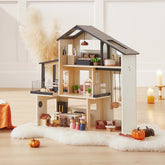 The Tiny Land® Sweetwood Edge Dollhouse by Tiny Land is displayed on a fluffy white rug with small pumpkins, candles, and pampas grass for a cozy autumn vibe. Miniature family models complete this inviting scene.