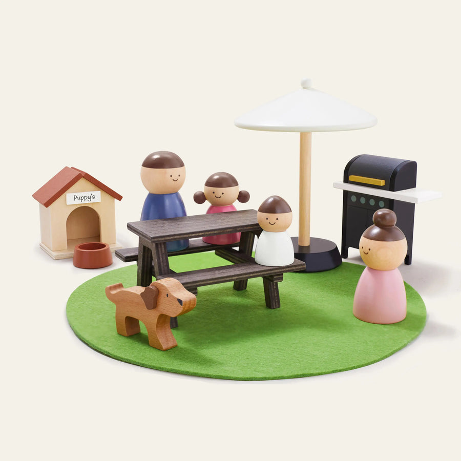 Wooden toy figures of a family, dog, grill, picnic table, and umbrella add charm to your Tiny Land® Sweetwood Edge Dollhouse—perfect for creating a cozy backyard barbecue scene in any modern dollhouse setup.