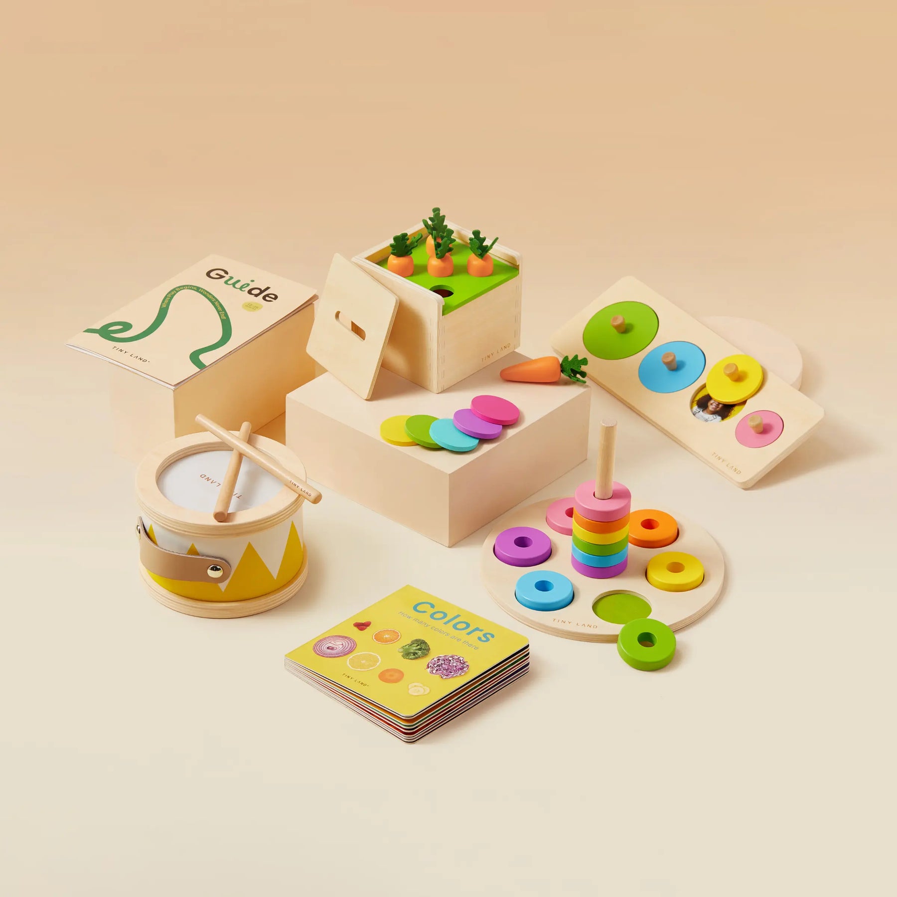 Tiny Land® Montessori Toys for Toddlers (13–15 Months) by Tiny Land features wooden educational toys—a drum, stacking rings, carrot garden puzzle, color-matching board, illustrated book, and guide—all on a light beige background.