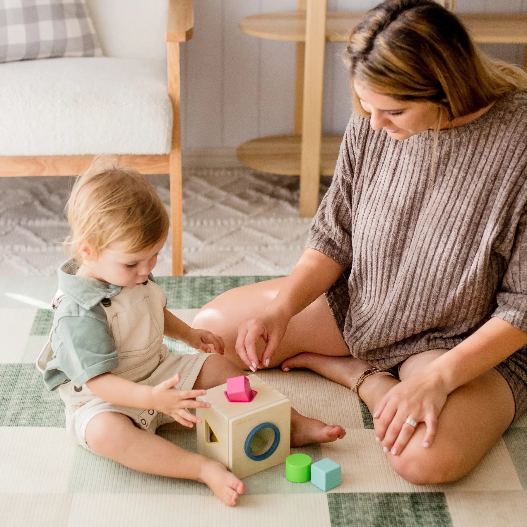 An adult and toddler play on a checkered mat with the Tiny Land® Montessori Advanced Skills Baby Set (13–24 months), enjoying sensory learning as they sort shapes together in a bright, cozy setting.