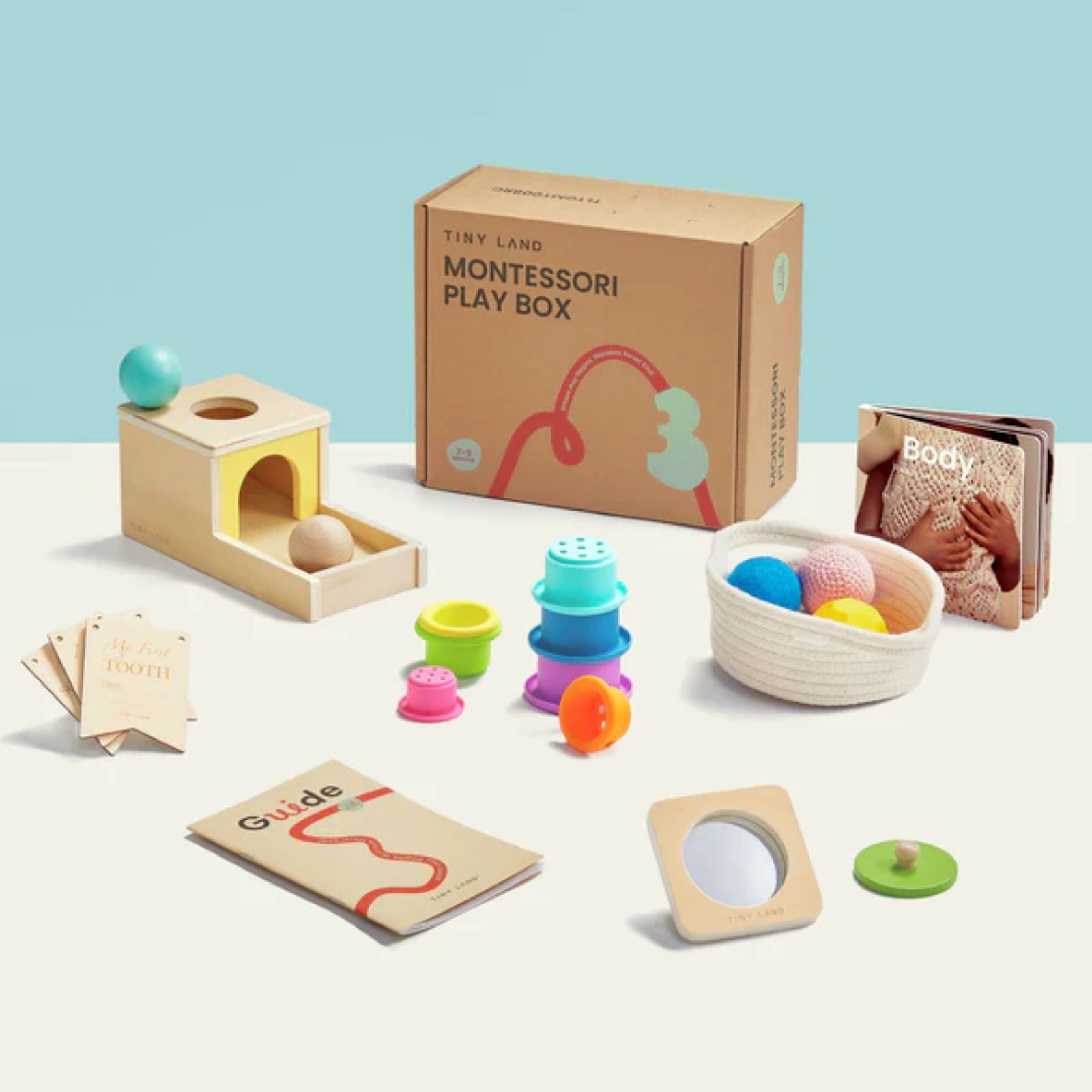 The Tiny Land® Montessori Toys - Various Stages set by Target includes a wooden ball drop, stacking cups, knitted balls with a basket, sensory discs, a soft book, activity cards, and a guide—all displayed on a light surface.