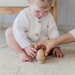 A baby in a white sweater sits on a cream carpet as an adult offers the Tiny Land® Montessori Toys for Infants (10–12 Months), sparking curiosity and discovery through Tiny Land’s baby development toys.
