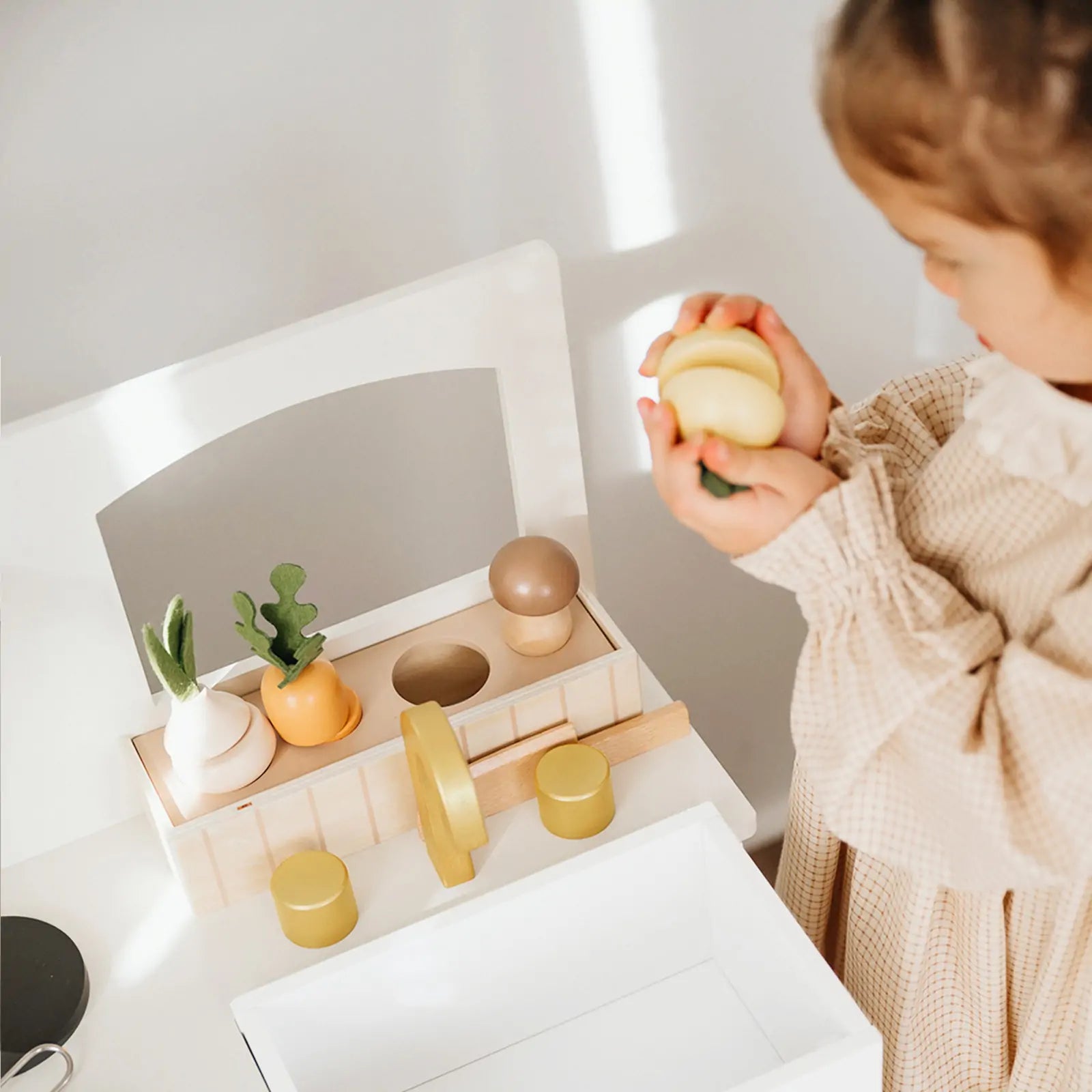 A young child enjoys imaginative play, preparing toy vegetables on the Tiny Land® Wooden Play Kitchen for Toddlers—Honey Kitchenette Pretend Cooking Set by Tiny Land|white