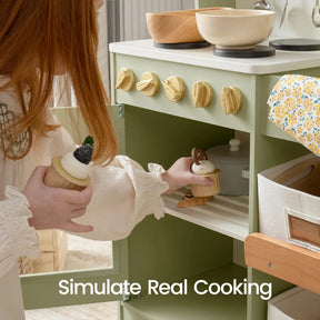 A child places toy cupcakes into the Tiny Land® Wooden Play Kitchen with Storage for Creative Toddlers, using pretend cookware from the kids kitchen set. Wooden knobs and pans by Tiny Land are visible, with the text "Simulate Real Cooking" appearing at the bottom of the image.|sage