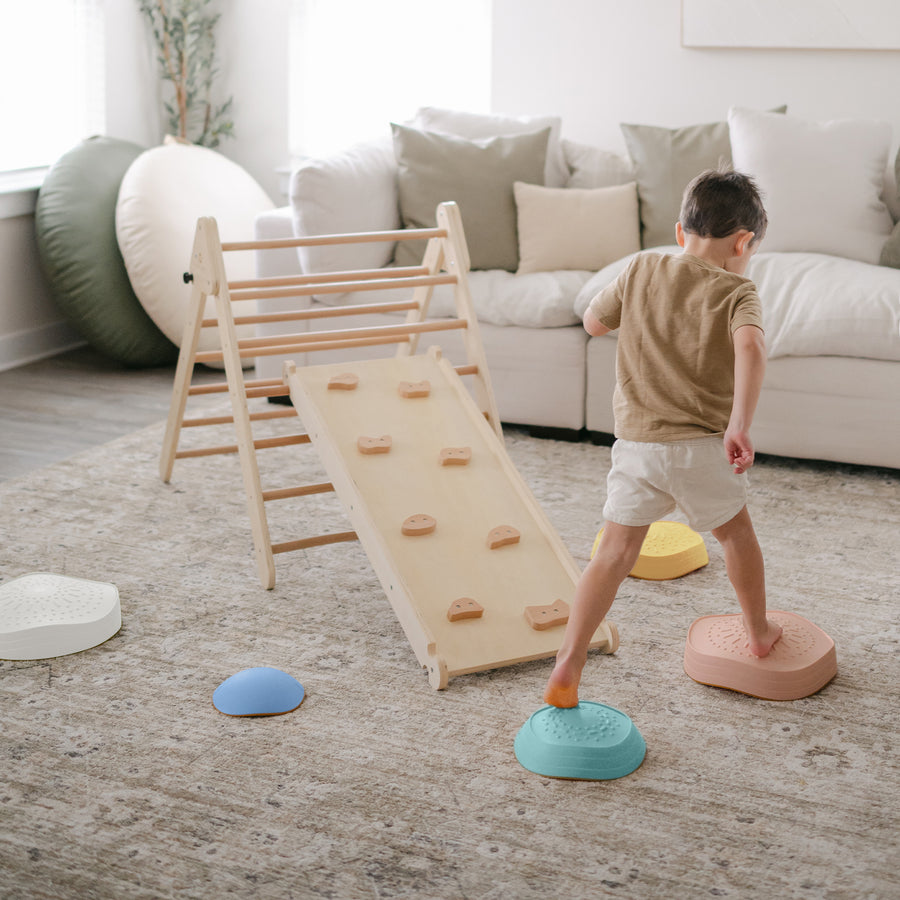 A young child steps on Tiny Land® Stepping Stones - Beach Vacation by Tiny Land, creating an indoor obstacle course toward a wooden climber with ramp in a cozy, well-lit living room to build motor skills.|Beach Vacation