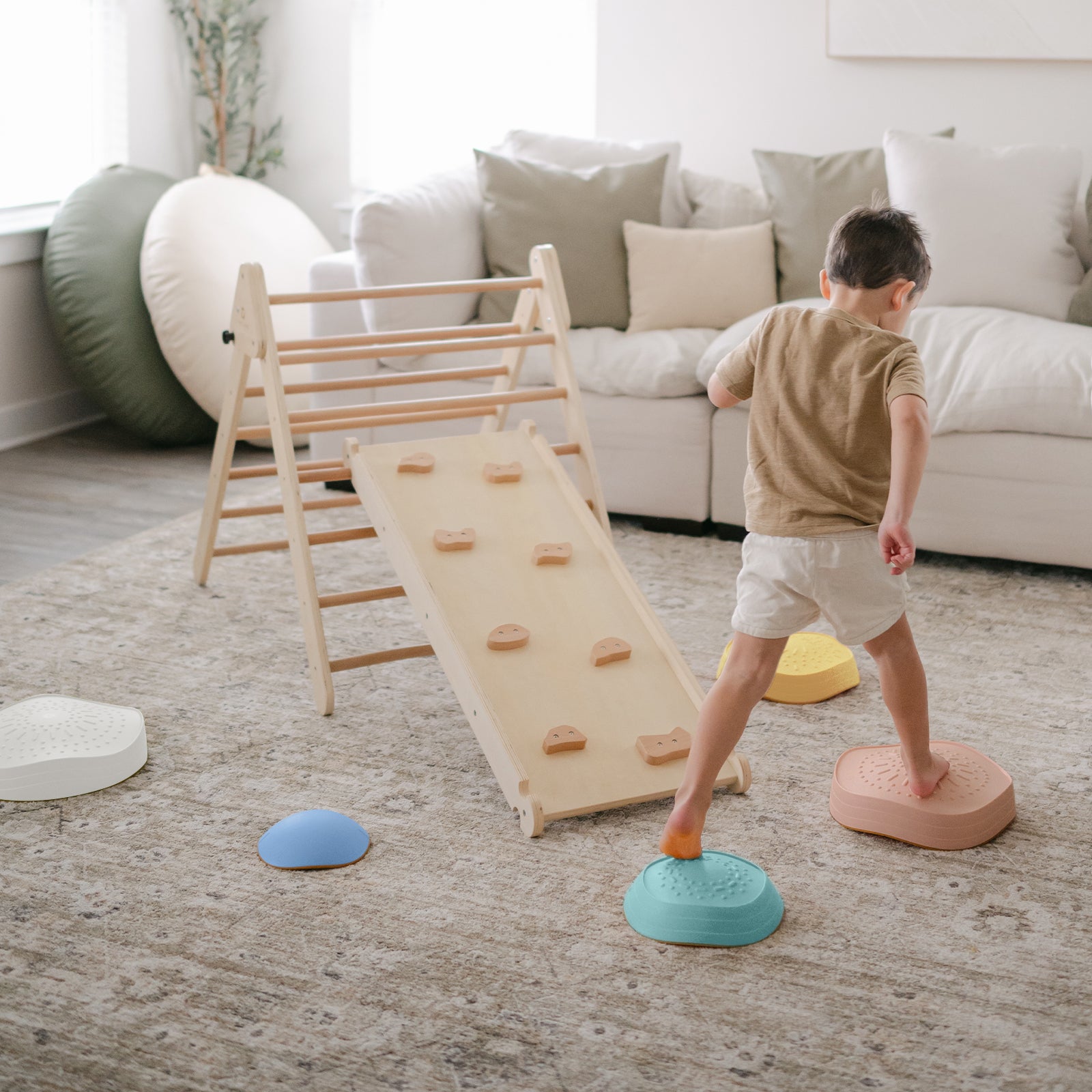 A young child steps on Tiny Land® Stepping Stones - Beach Vacation by Tiny Land, creating an indoor obstacle course toward a wooden climber with ramp in a cozy, well-lit living room to build motor skills.|Beach Vacation