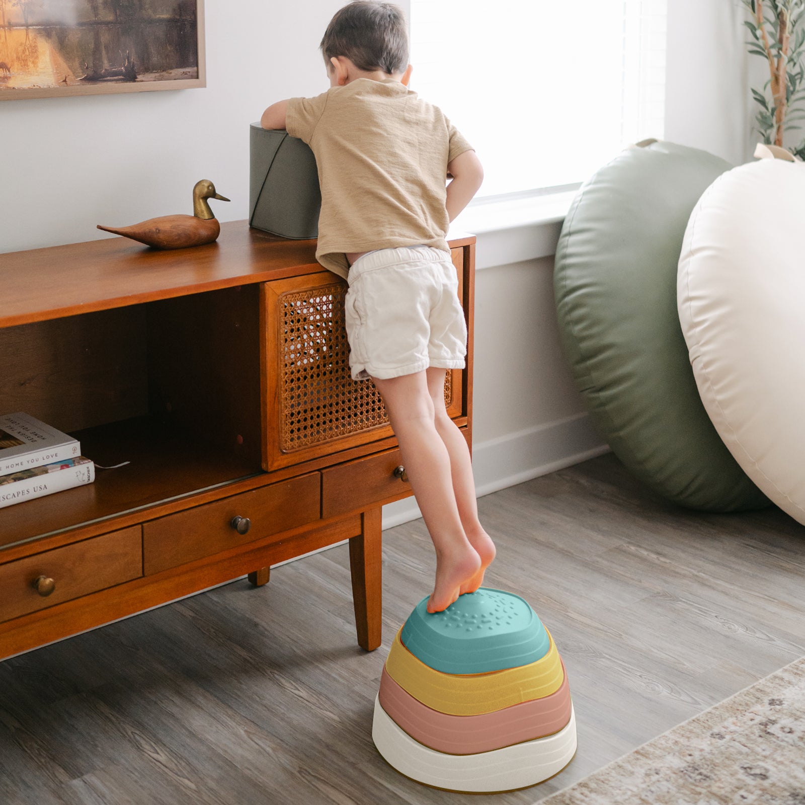 A young child stands on Tiny Land® Stepping Stones - Beach Vacation by Tiny Land, reaching for an object on a console table in a bright living room—ideal for building motor skills through this fun obstacle course.|Beach Vacation