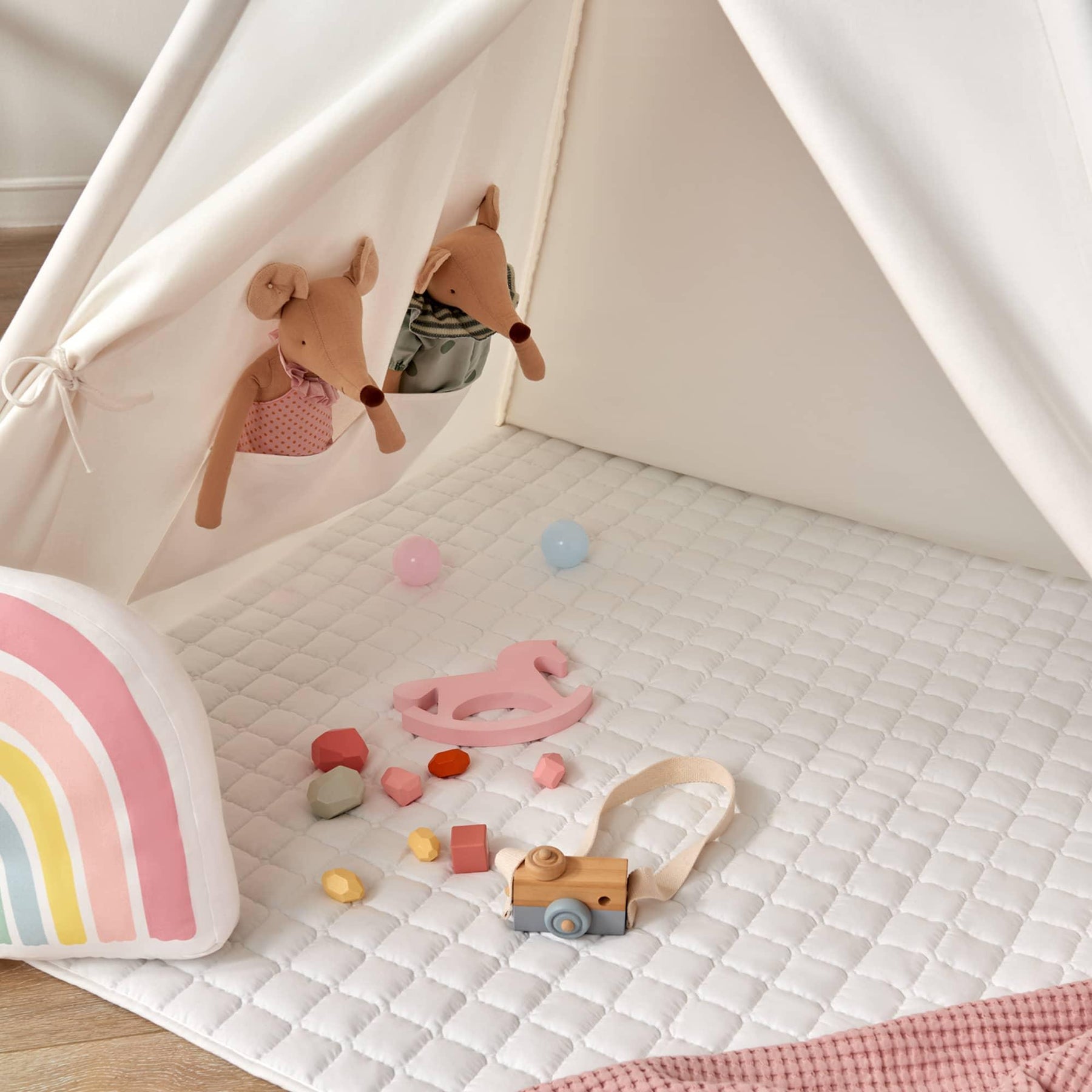 The Tiny Land® Teepee Tent for Kids with Mat features a cozy white quilted floor mat, pastel blocks, a pink wooden bird, a toy camera, two stuffed animal mice in pockets, and a rainbow pillow—perfect for indoor play.