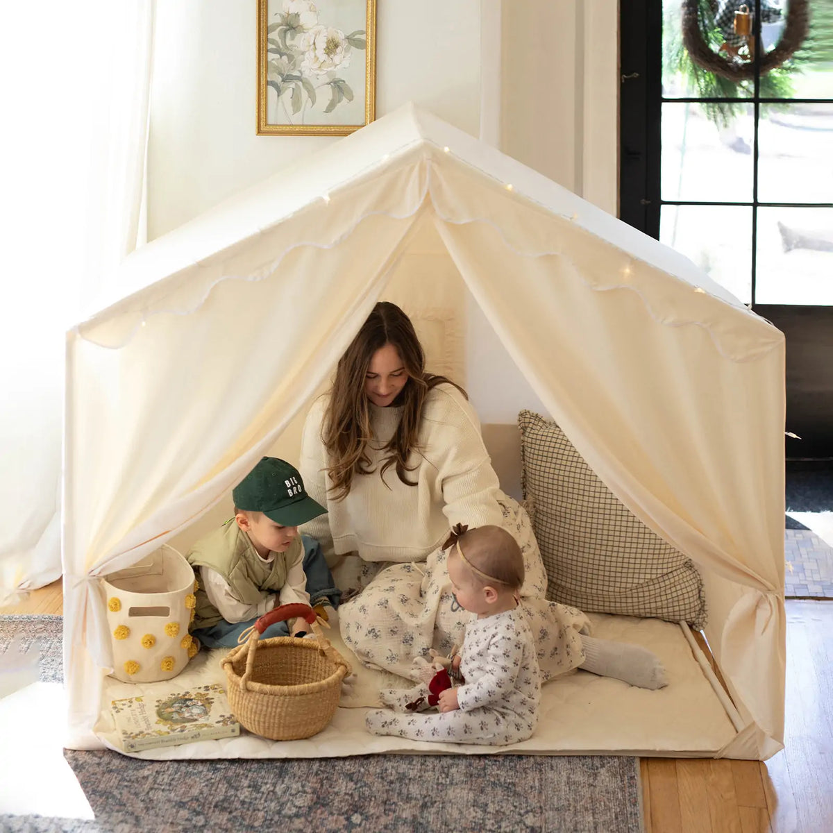 A woman and two children play with toys on a quilted mat inside the spacious Tiny Land® Kids Tent – Large Cozy Tent with Star Lights, enjoying warm natural light for cozy, inviting playtime.|fabric